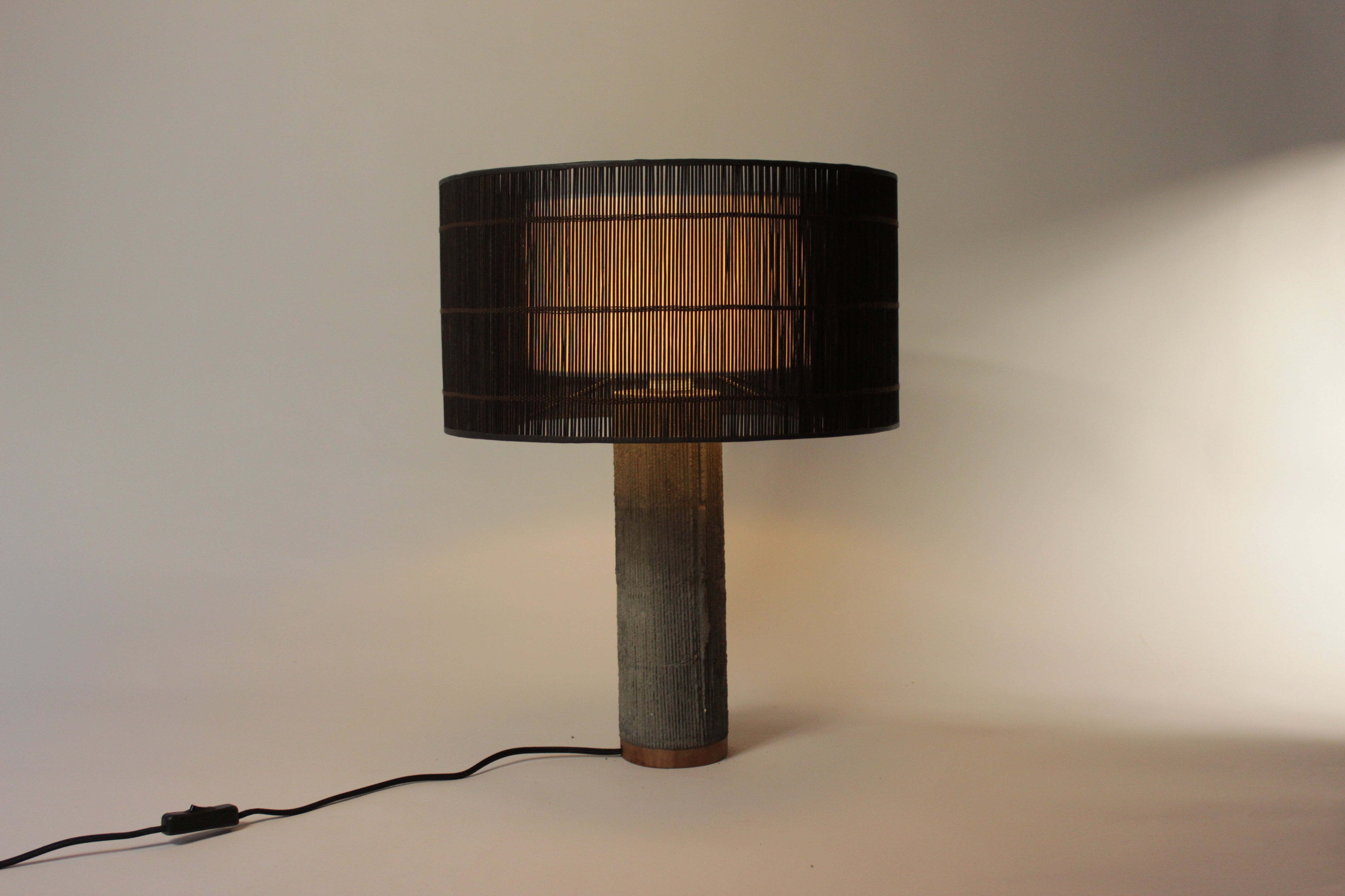 Stijlvolle lamp met donkerbruine geweven kap en betonnen voet in rustige tint.
