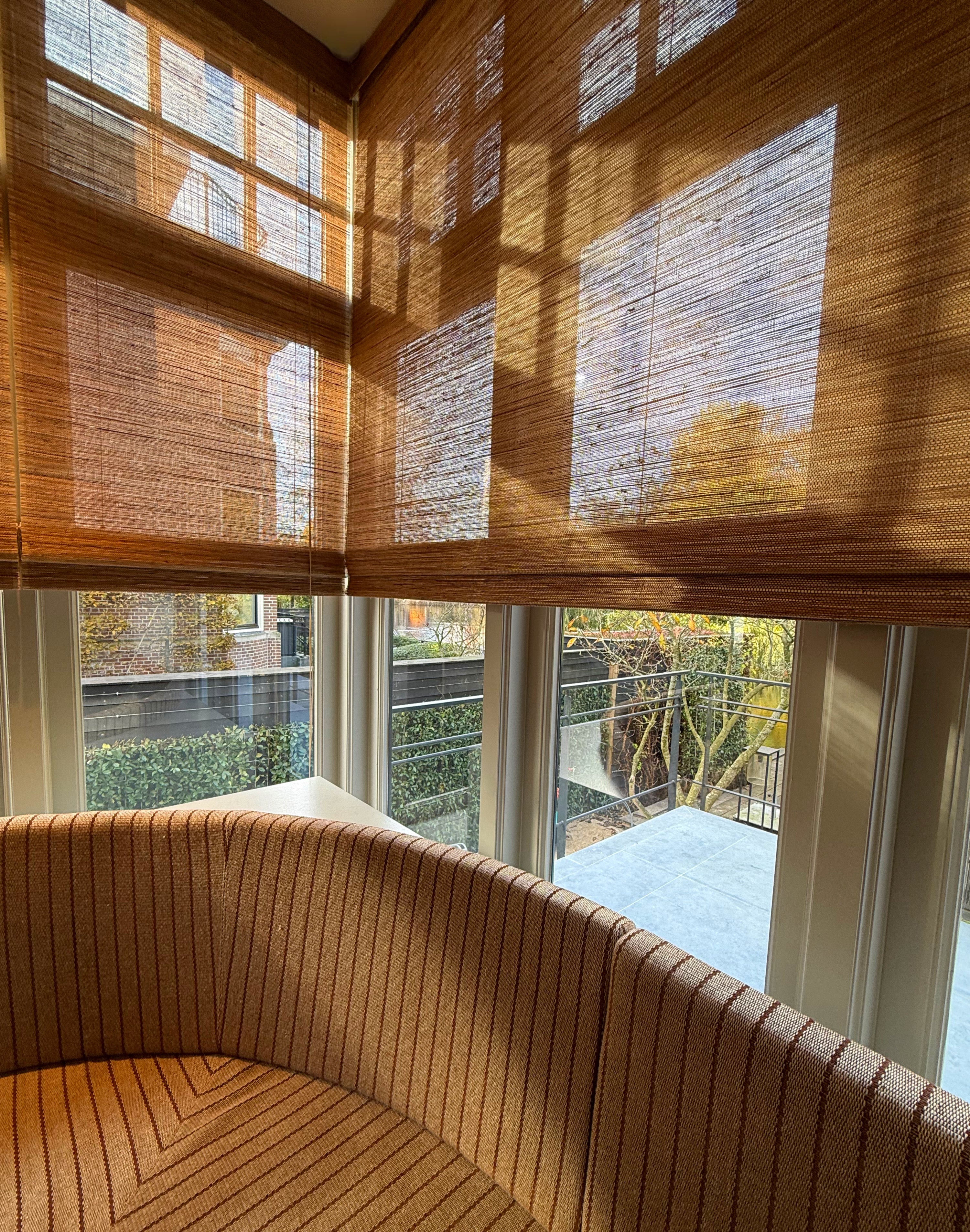 Folding Tuamoto blinds met natuurlijke lichtval en zachte schaduwen in een hoekraam.
