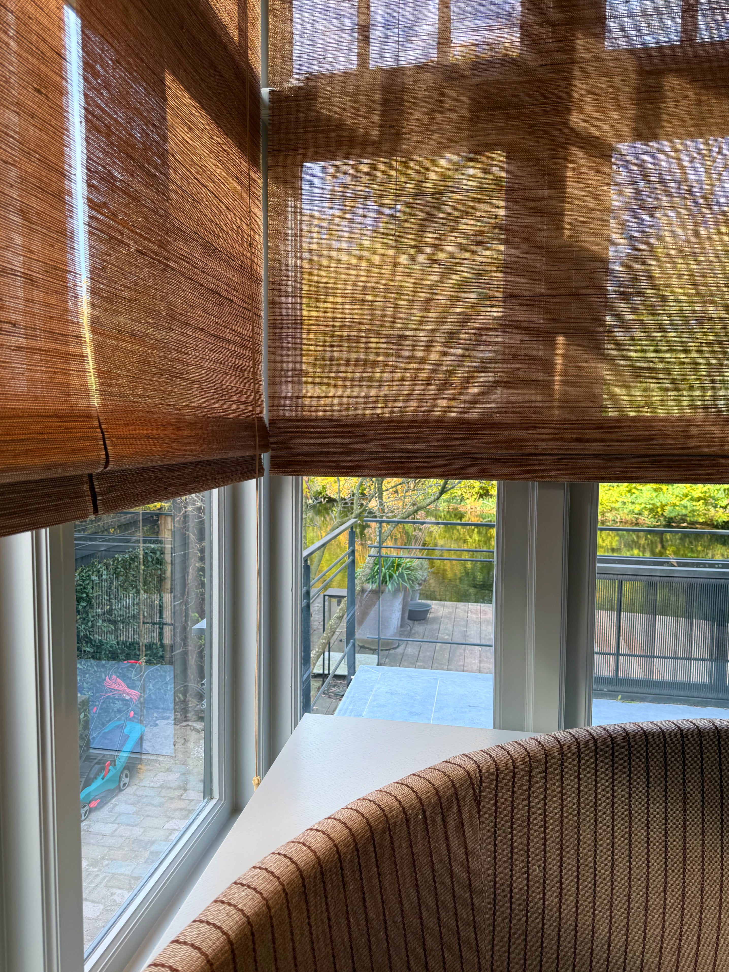 Vouwblinds van Tuamoto die zacht daglicht filteren met uitzicht op tuin en zithoek.